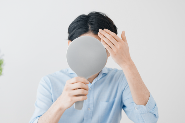 鏡で頭皮を見て気にしている男性の写真